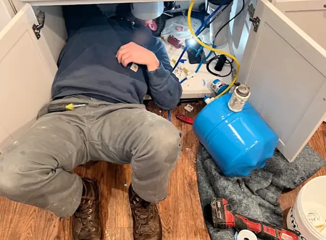 Plumber working under a kitchen sink on a water filter