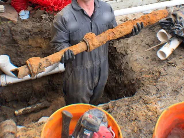 Plumber holding a rusted old cast iron sewer pipe dug out of a trench